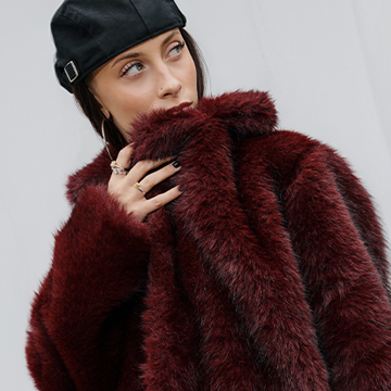Naine burgundia karusnahkmantlis ja musta nokkmütsiga, poseerib streetwear stiilis. banner